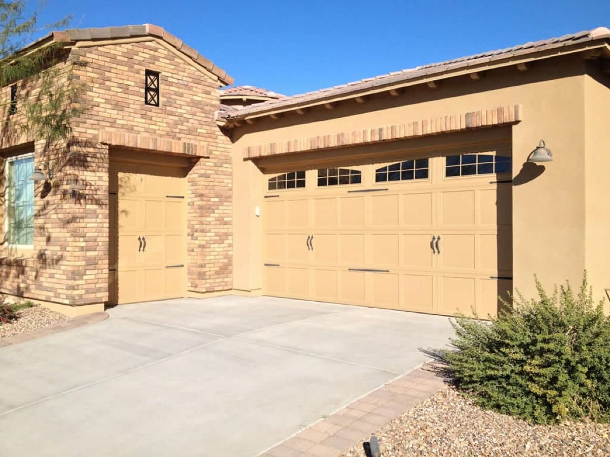 Two matching beige garage doors on a brick house