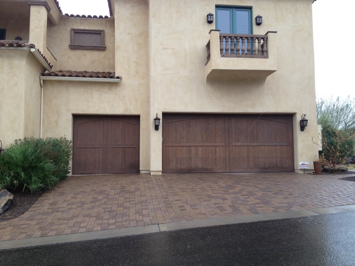 Two brown matching garage doors on a beige stucco house with a paved driveway