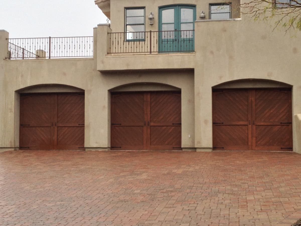 Three wood-finish single garage doors on a beige stucco building with a paved driveway