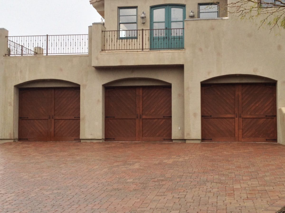 Three wood-finish single garage doors on a beige stucco building with a paved driveway