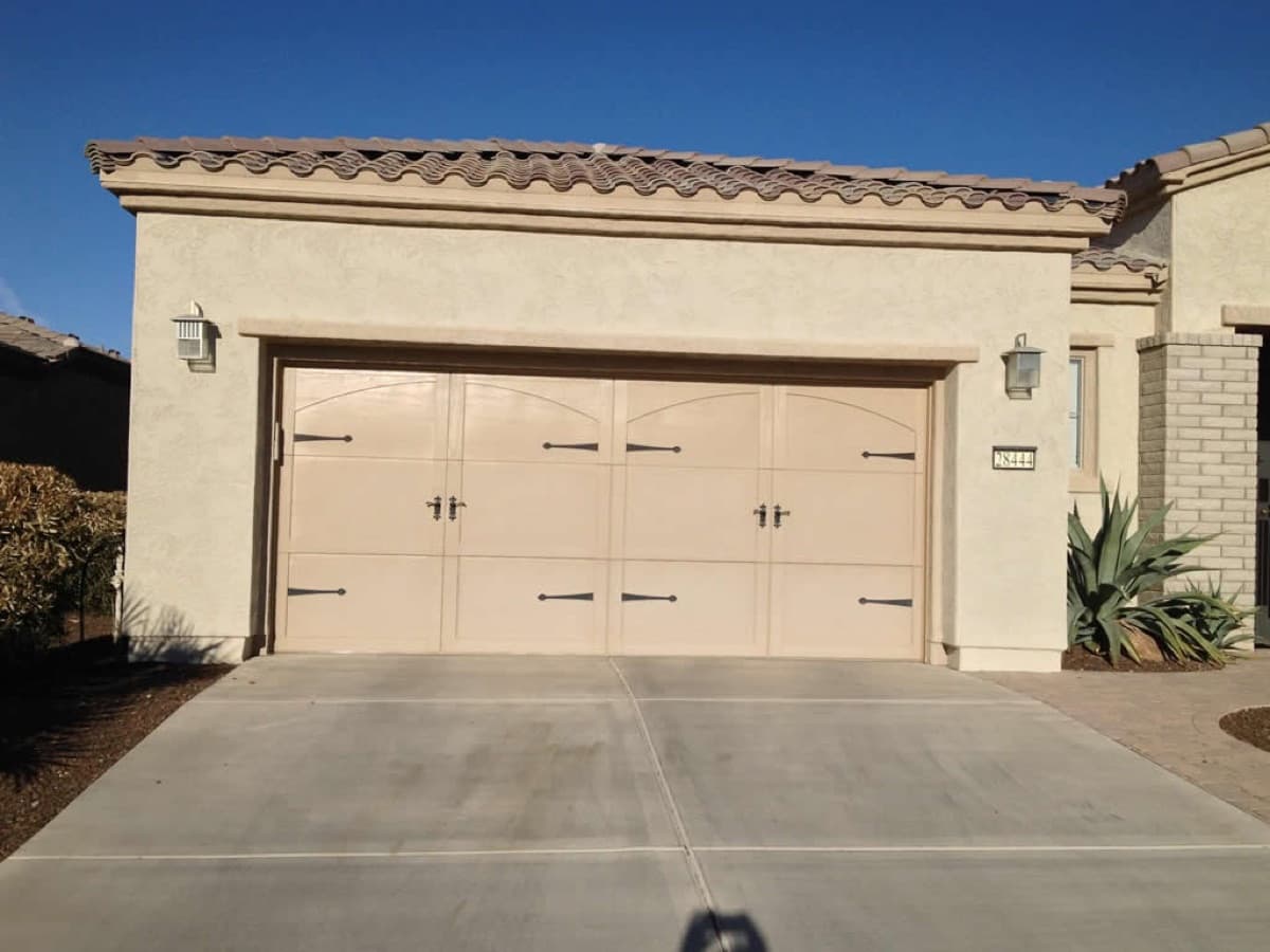 Wide beige custom two-car garage door on a stucco house under a clear sky