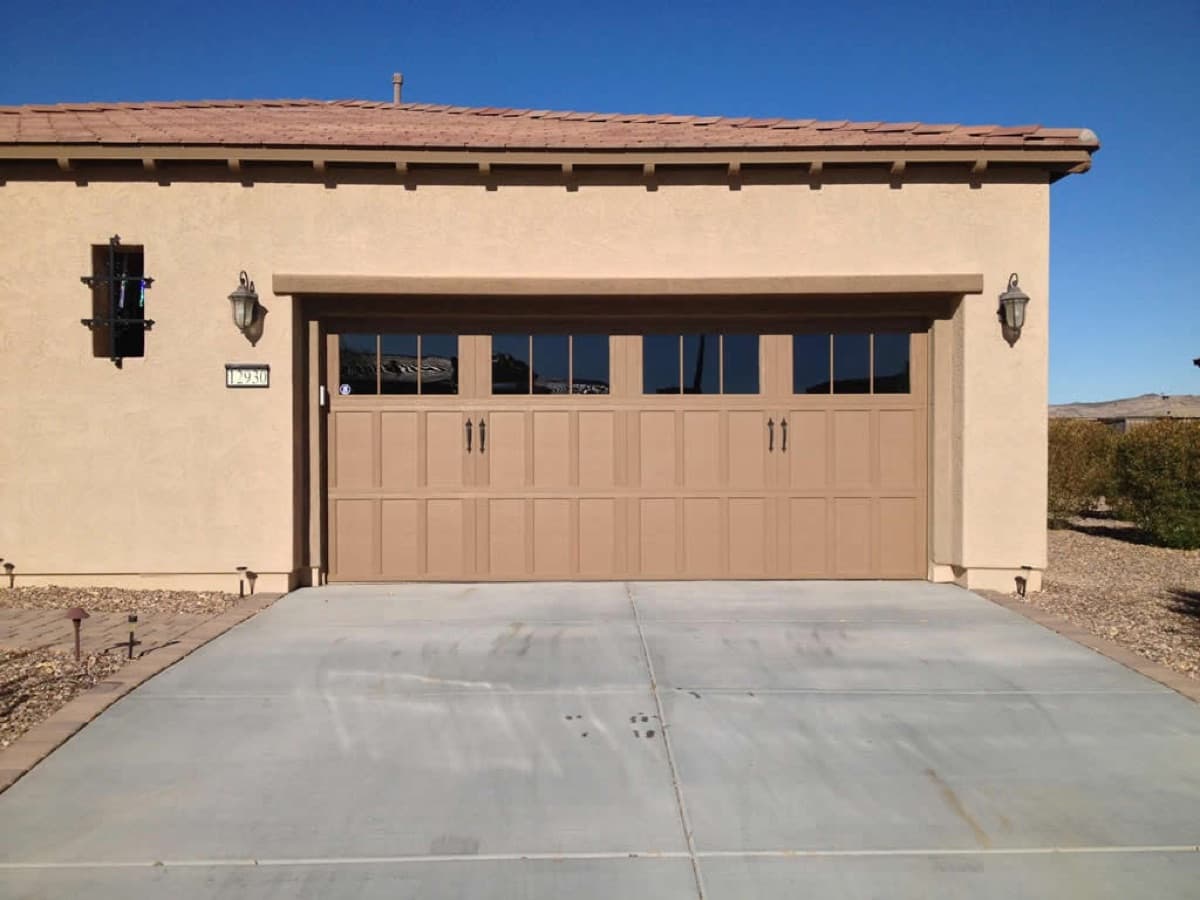 Beige sectional garage door with a row of windows across the top panel, on a stucco home