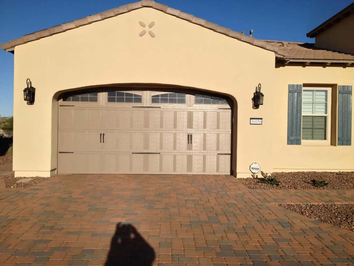Beige garage door on a stucco house with a brick paver driveway