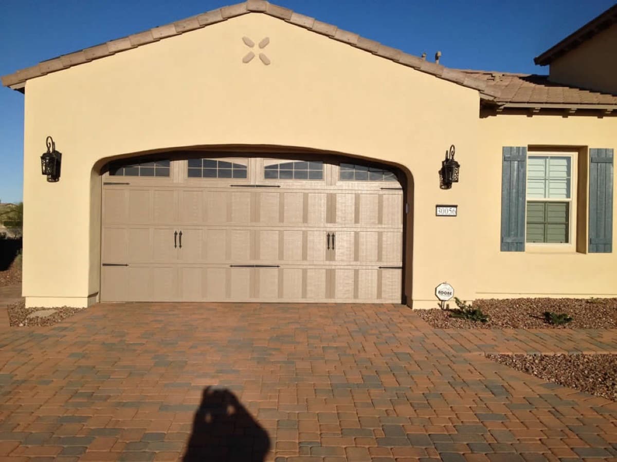 Beige garage door on a stucco house with a brick paver driveway