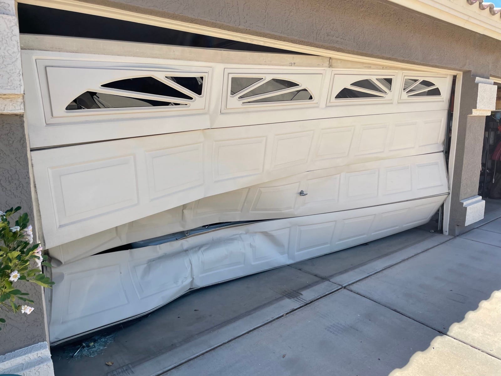 A residential garage door buckled out of shape and hanging out of its opening