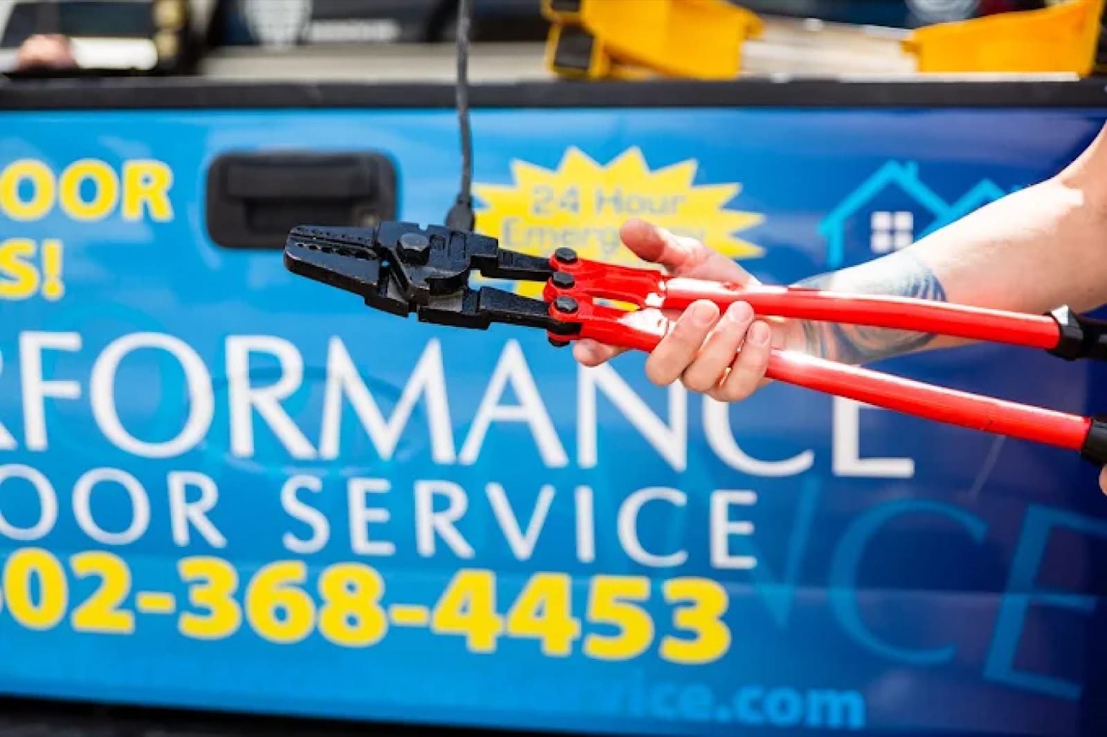 A Performance Door Service technician holding bolt cutters beside a wrapped service truck