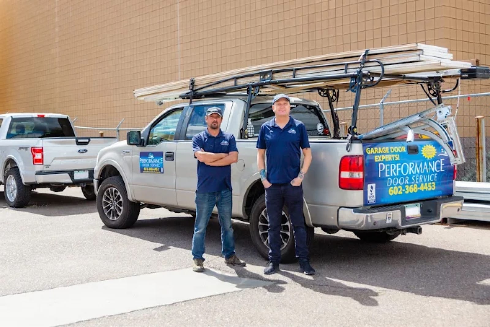 Two Performance Door Service technicians beside their wrapped trucks, loaded with garage door sections